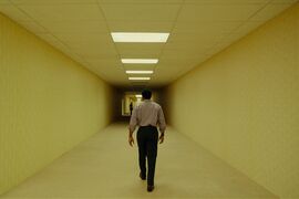 A man walks along a long corridor towards a spooky figure.