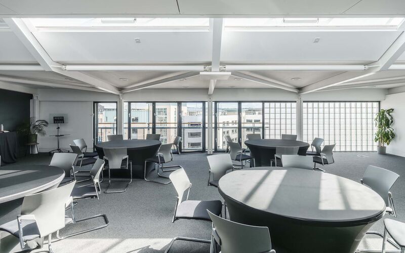 A room filled with circular tables the light from windows on the ceiling floods down