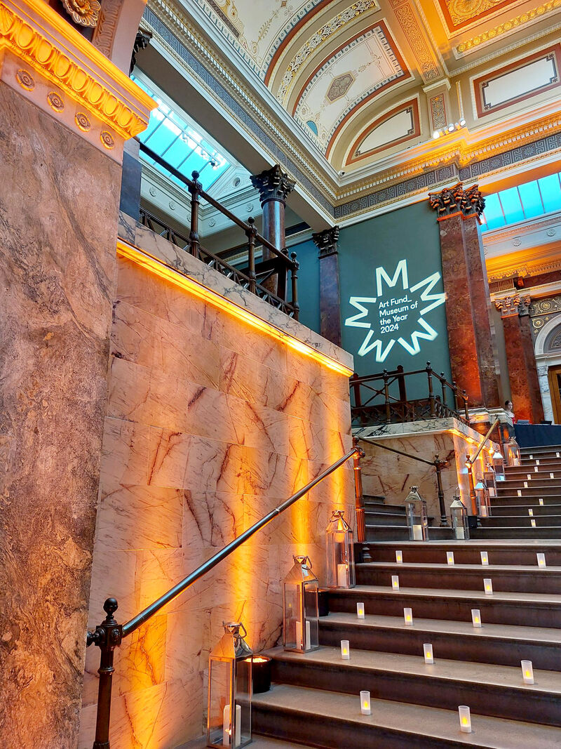 Stairs lit up by candles with Art Fund Museum of the Year branding being displayed on wall