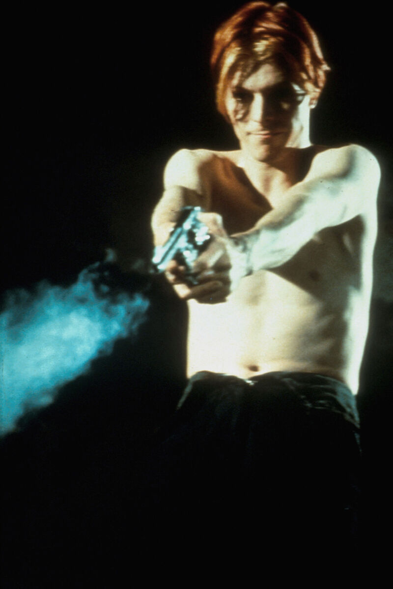 A shirtless man fires a gun