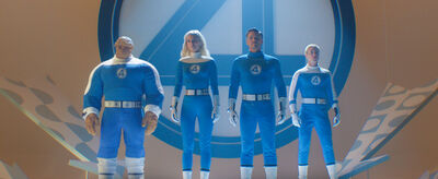 Three people and one man made out of rocks stand behind a giant number 4, all wearing blue suits with the number 4 on them.