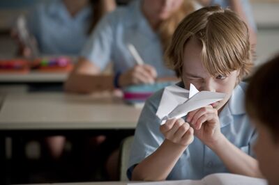 A boy in a classroom is ready to throw a paper plane
