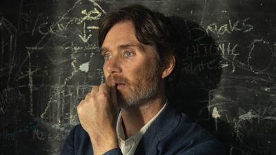 A man with a beard leans against a blackboard, looking pensive.