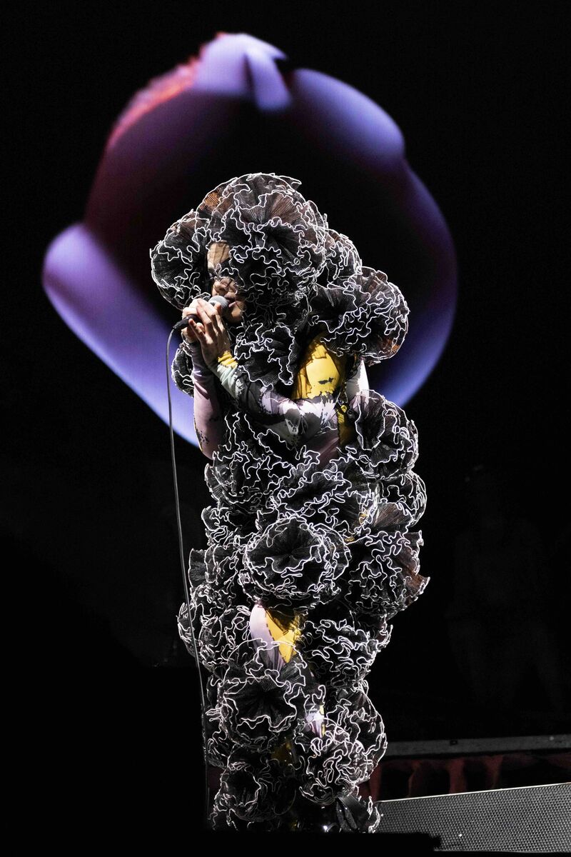 Bjork sings on stage wearing a complicated, black ruffled costume,.