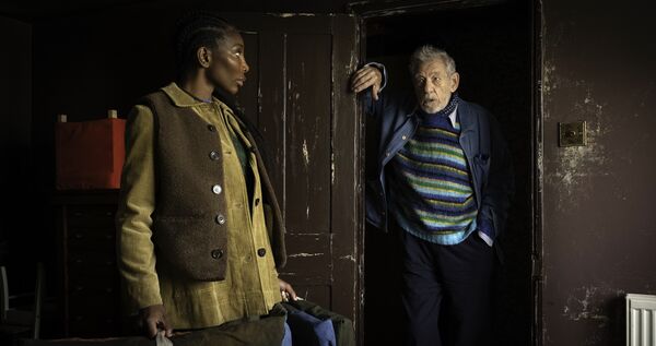 A young woman and older man stand in an art studio.