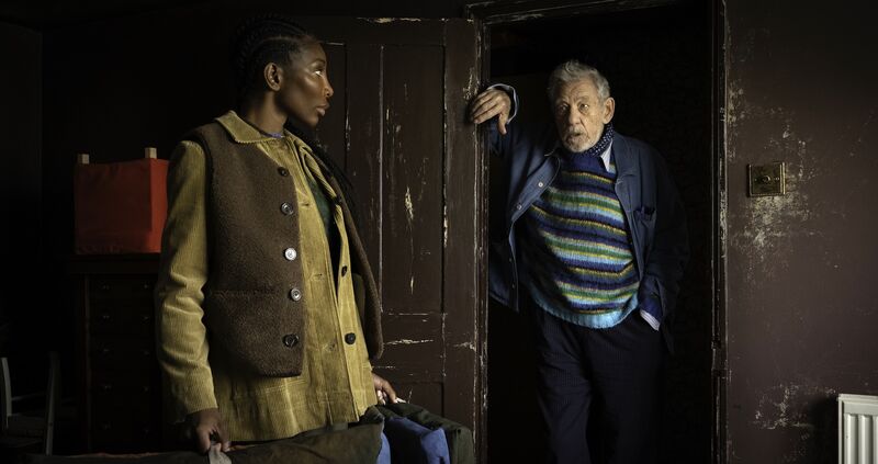 A young woman and older man stand in an art studio.