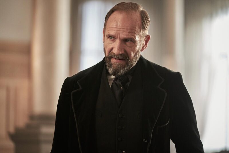 A middle-aged man with a beard and moustache, wearing a choir master's suit