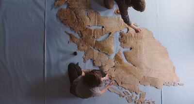 A top-down view of two people constructing a map out of old paper.