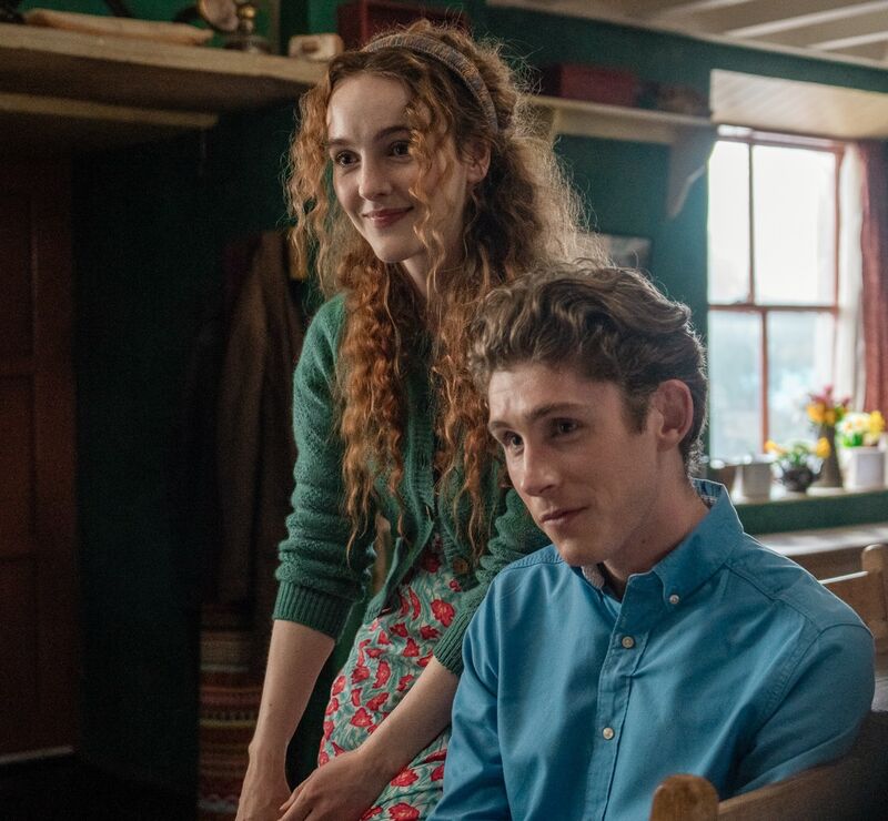A young man and woman sit together smiling in a cottage.