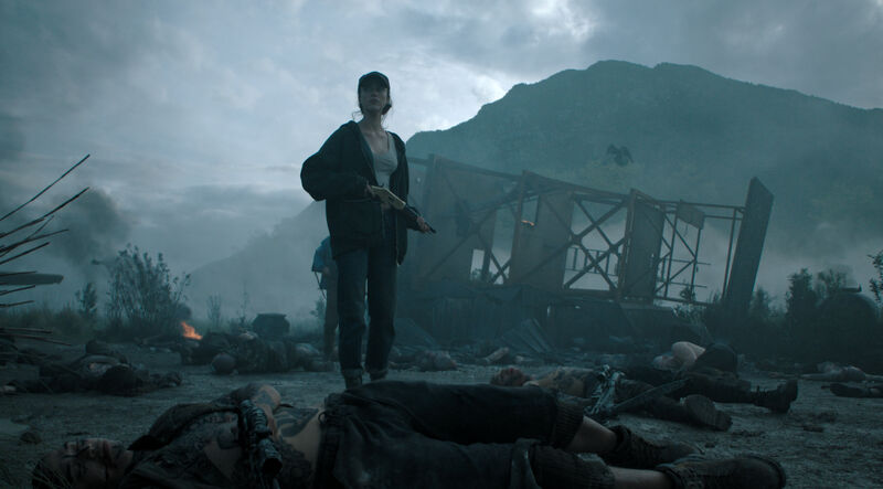 A young woman holding a gun stands in a smoldering destroyed scene surrounded by bodies