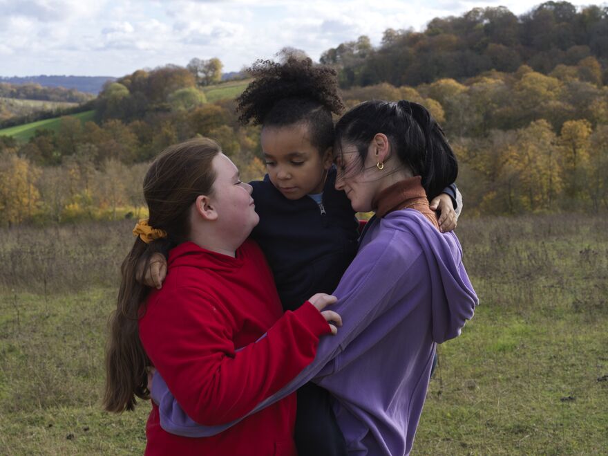 A woman hugs two little girls in a field.