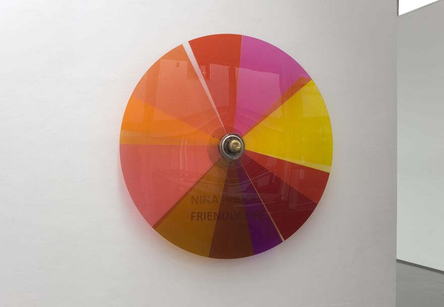 A wheel which can be spun at Nina Rhode's exhibition. The wheel is plastic and has different warm pink, red and orange colours on it in segments.