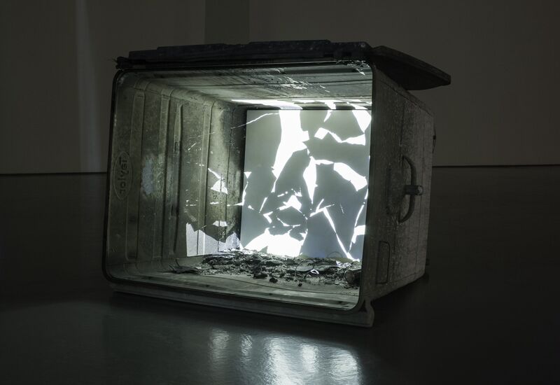 From Navid Nuur's exhibition. A large metal recycling bin is toppled over. The bottom of the bin is filled with light and broken glass.