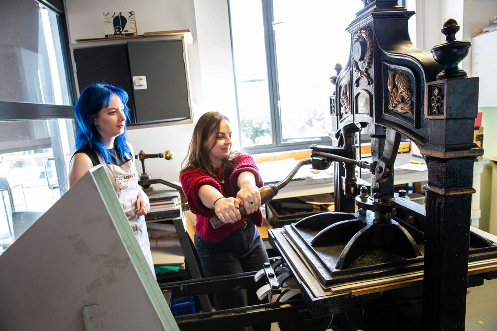 Person printing a lino cut using a printing press