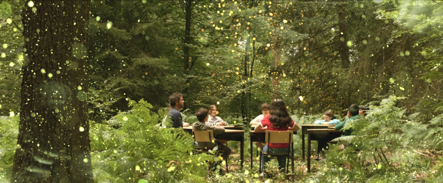 A green forest space in the centre a group of children sit around a table 