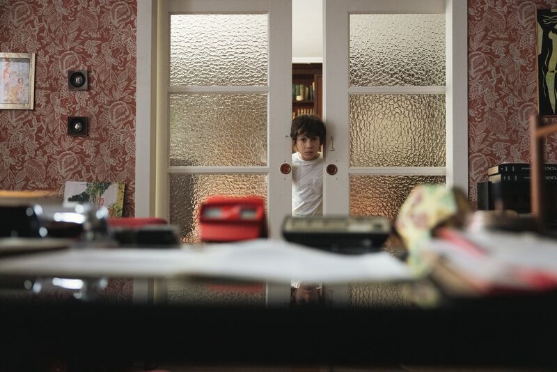 A young boy peeks through a set of frosted double doors.