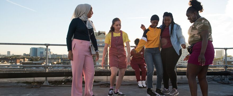 A group of teen girls dance on a city rooftop
