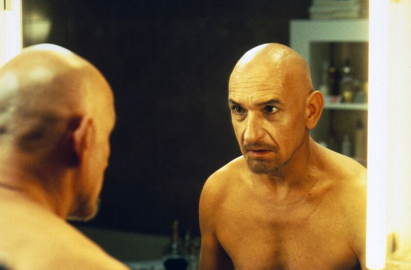 Bald, bearded Ben Kingsley looks in a mirror