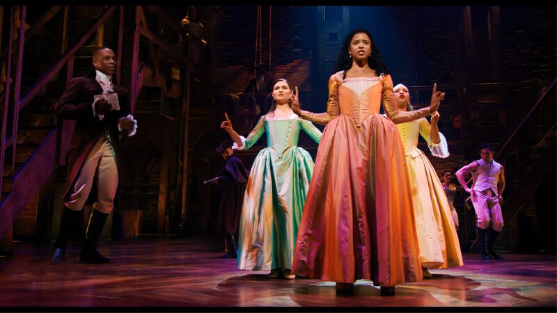 Three women in 18th century dresses dance on stage