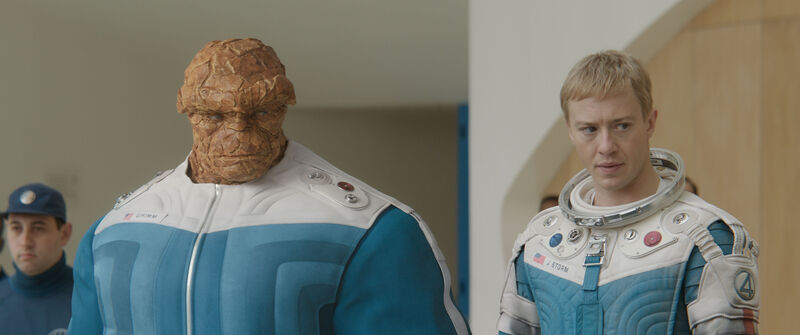 A young man with blonde hair wearing a blue and white suit stands next to a humanoid creature with rocks for skin.
