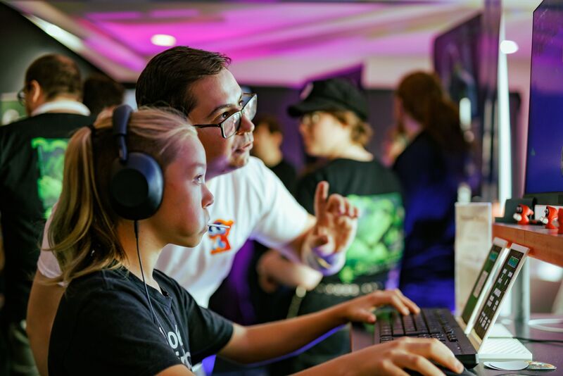 A person shows a child wearing headphones how to play their game at Drop in and Play