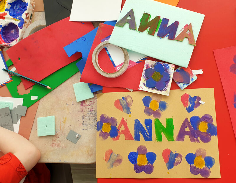 Table covered with stamp making supplies and artwork that says 'Anna' surrounded by hearts and flowers