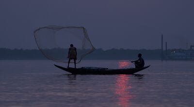 Two figures on a fishing boat at sunrise, a fishing net thrown in the air.
