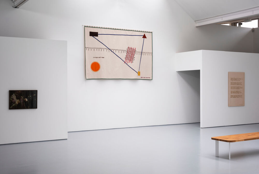 A gallery space with a large fabric banner on the far wall also visible are two entrances to a darkened space. Two further images are visible on walls either side.