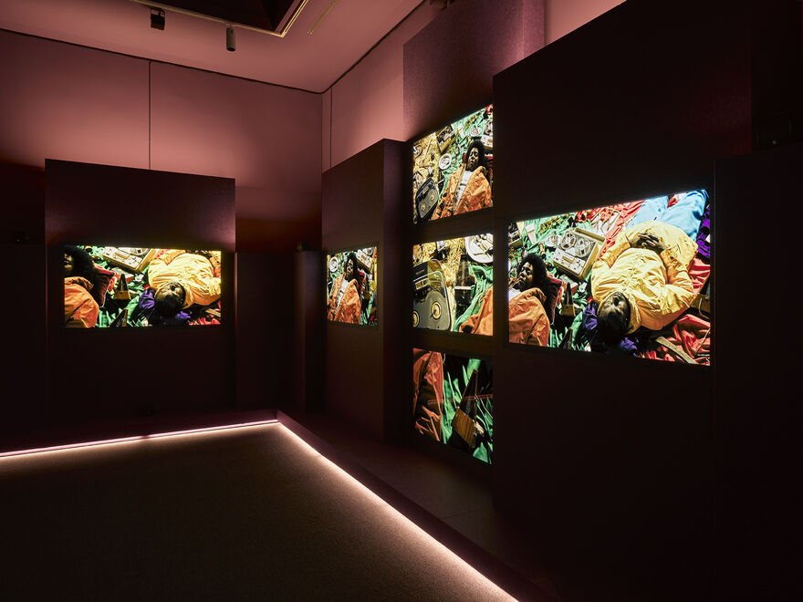 a dark gallery space red lighting pushes up with screens on the wall 