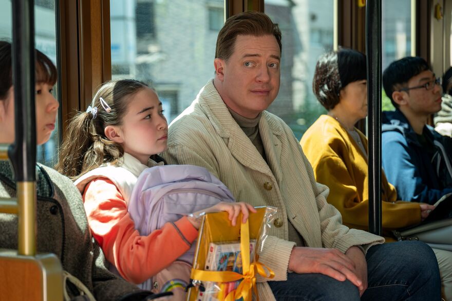 A man and a little girl sit next to each other on a busy train