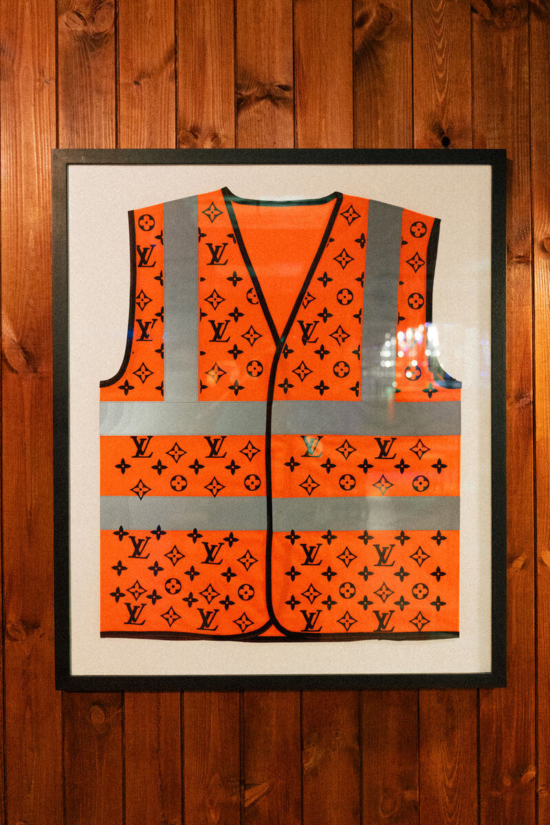 A high-vis vest in a frame decorated with Louis Vuitton-like  logos 