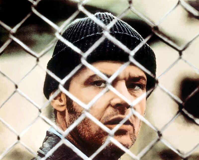 A man wearing a winter hat looks through the barbed wire of a fence