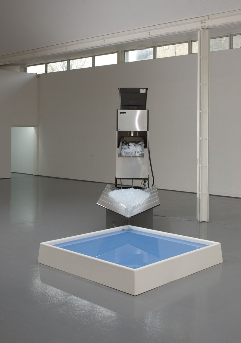 From Spencer Finch's exhibition. A machine produces ice, which is held above a small blue container filled with water.