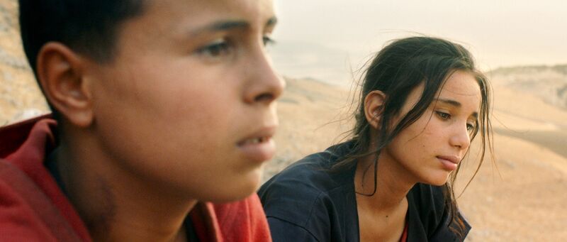 Two serious-looking teenagers sit in a desert.