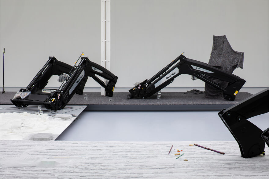 A gallery setting, with large farm equipment sitting on a low plinth. details of other small objects just visible