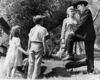 Two children stand holding hands and looking at a man and woman