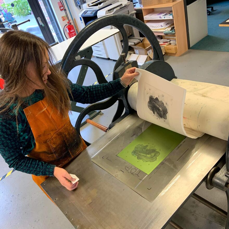 Photo of Claire McVinnie taking a print off of a press in DCA Print Studio