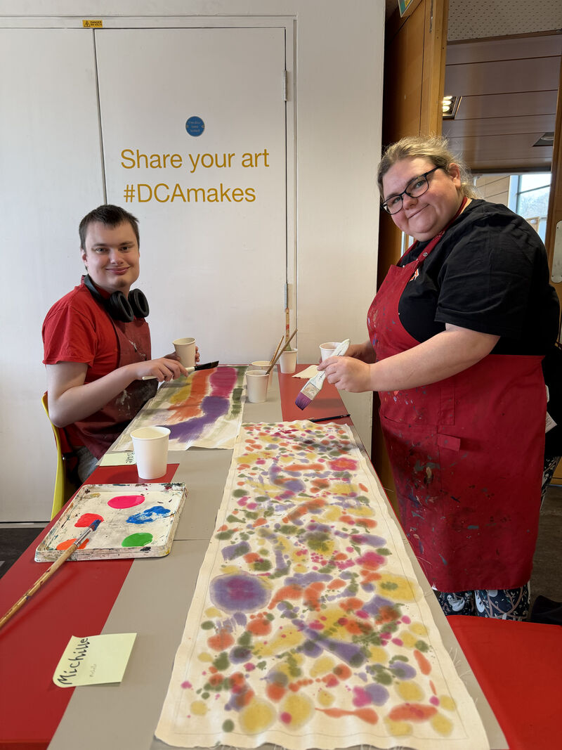Two people at a table painting fabric to make lampshades