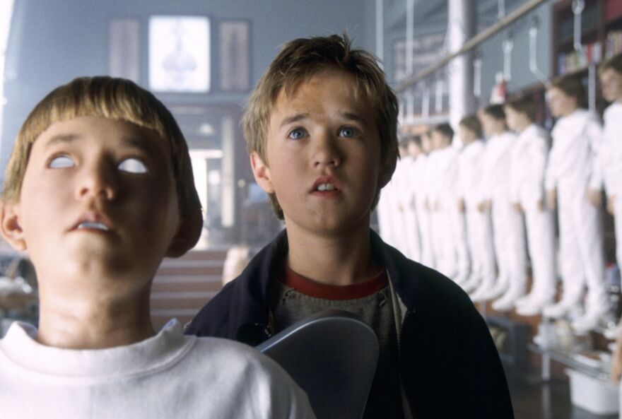 An android boy among lots of android parts in a factory.