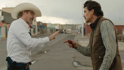 A man with a cowboy hat argues with another man on an empty town street.