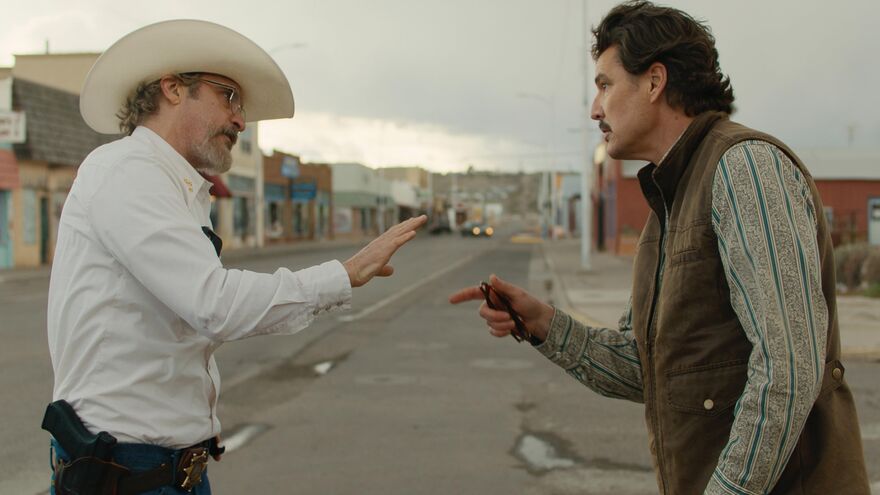 A man with a cowboy hat argues with another man on an empty town street.