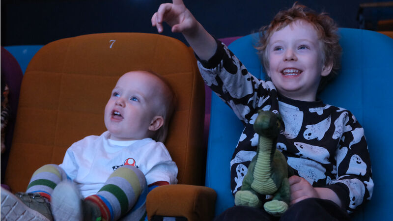 Two children in the cinema. One is pointing at the screen and they are both smiling