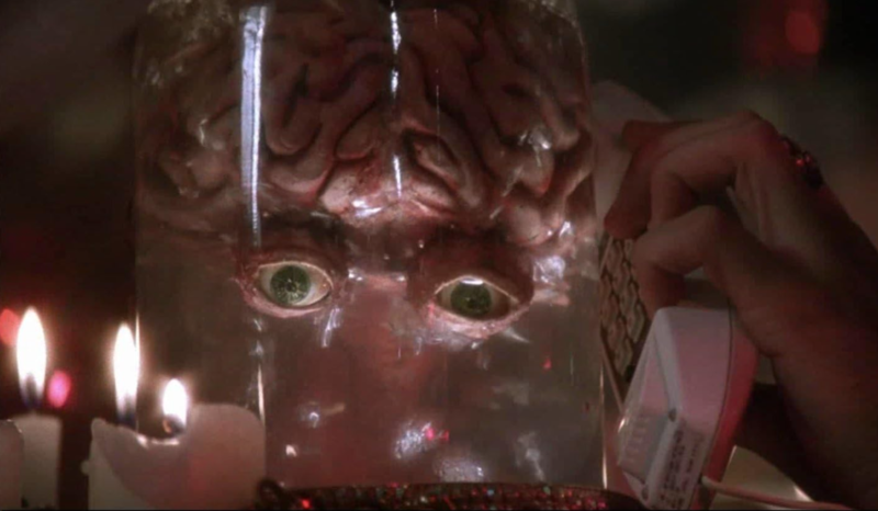 A jar containing a brain with eyes. A hand holds a phone up to the side of the jart