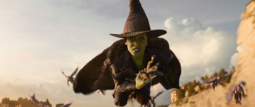 A green-skinned woman flies on a broomstick.