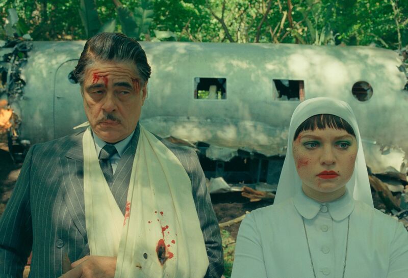 A man with blood on him and a broken arm stands next to a nun wearing white, behind a plane wreck,