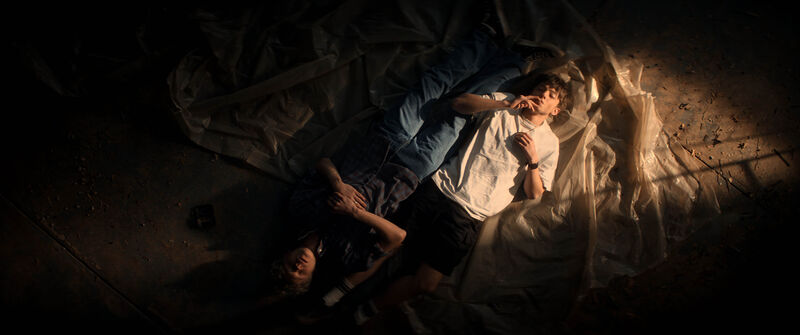 Two teenage boys lie on a mattress, while one stares at the ceiling