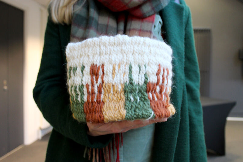 Woven plant pot holder with green, yellow and rust coloured design. Created using peg loom weaving.