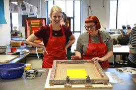Two people smiling as they prepare a screen for printing in DCA Print Studio