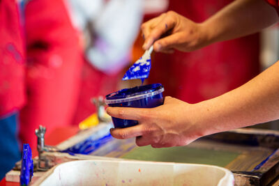Close up of hands holding a tub of blue ink and a spatula