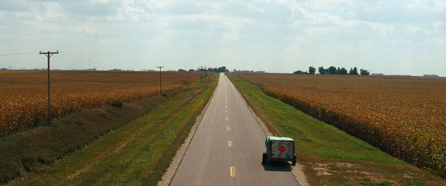 A long straight road, with a tractor and trailer parked in a lay-by